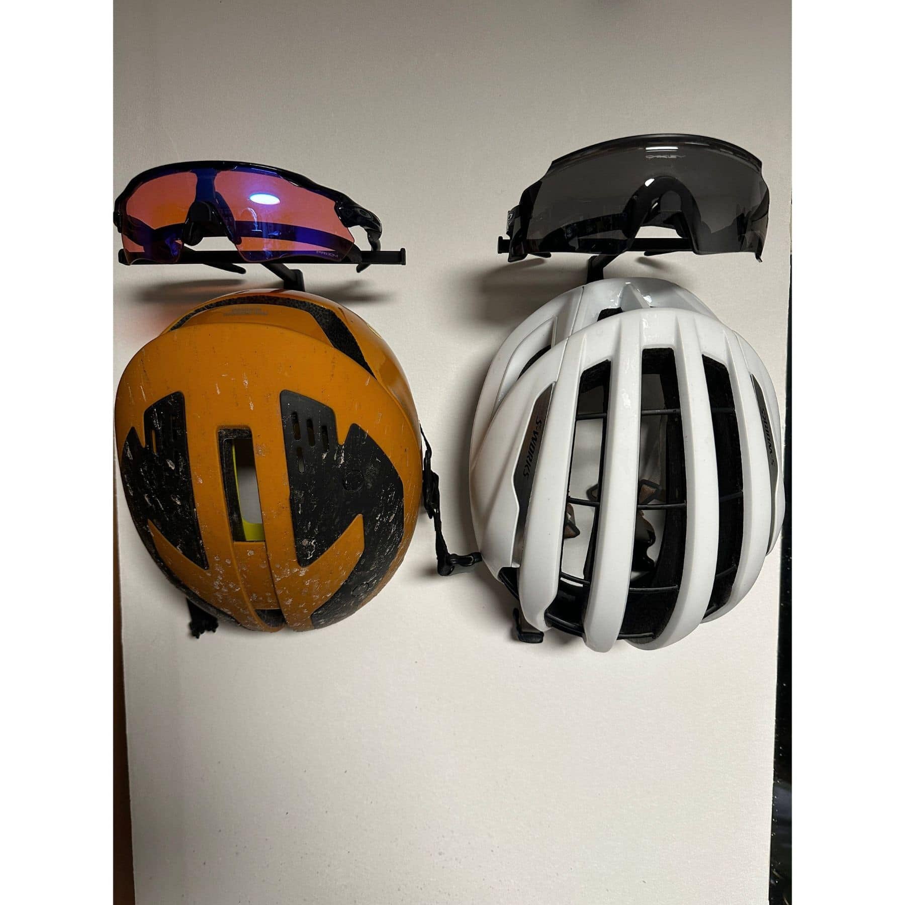 Two wall mounted helmet and glasses hangers with cycling helmets and Oakley sunglasses